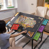 A person is assembling a large tilting puzzle board with multiple storage drawers on a table.