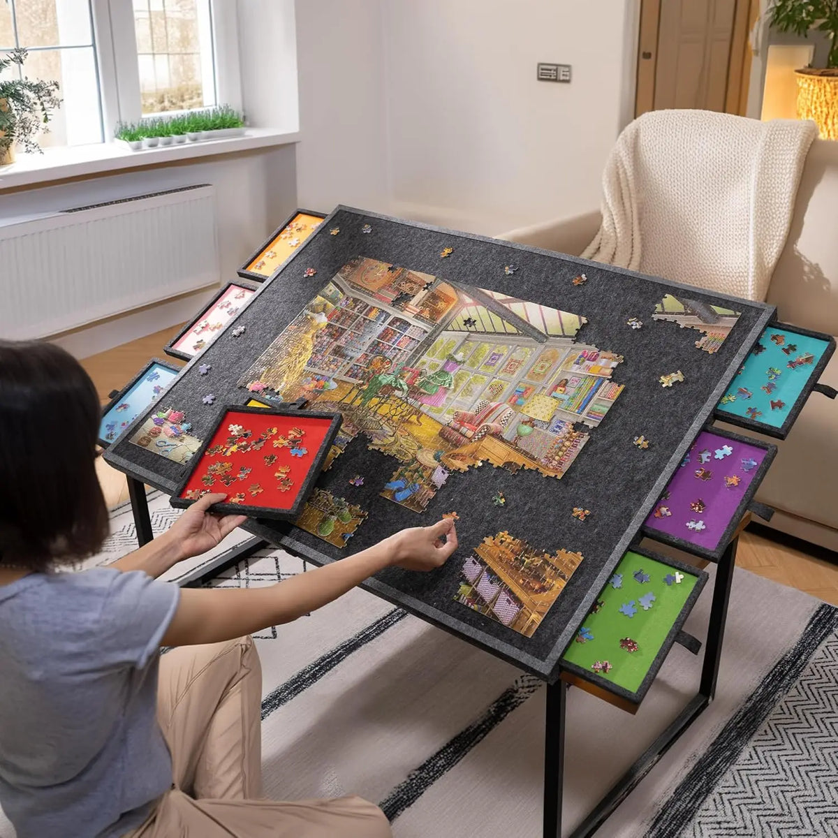 A person is assembling a large tilting puzzle board with multiple storage drawers on a table.