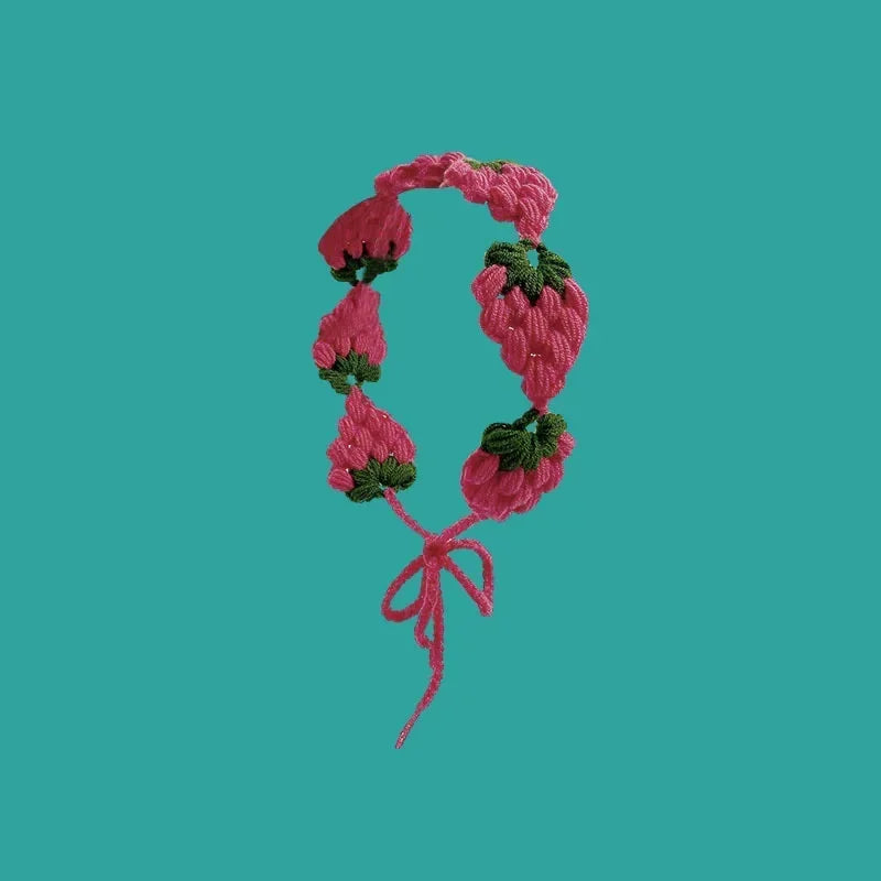 A pink strawberry crochet headband with a wide elastic band against a teal background.