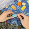 Hands are holding small plastic containers filled with various colored beads and craft supplies on a blue patterned fabric.