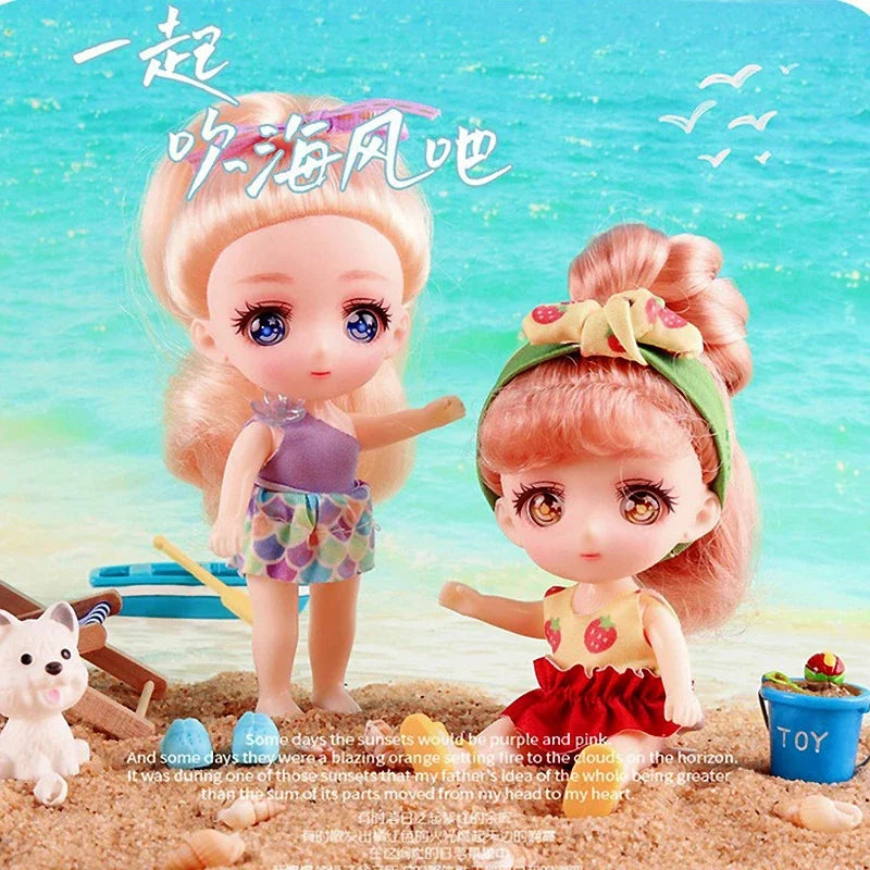 A pair of pink-haired mini dolls in colorful outfits standing on a sandy surface with a sea background.