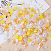 A scatter of mixed resin rhinestone pearls in yellow, gold, and iridescent finishes for craft and nail art.