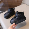 A close-up view of black toddler winter snow boots with a quilted texture and soft sole being held by a hand.