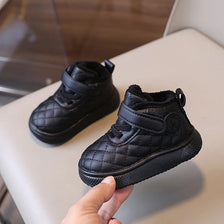 A close-up view of black toddler winter snow boots with a quilted texture and soft sole being held by a hand.