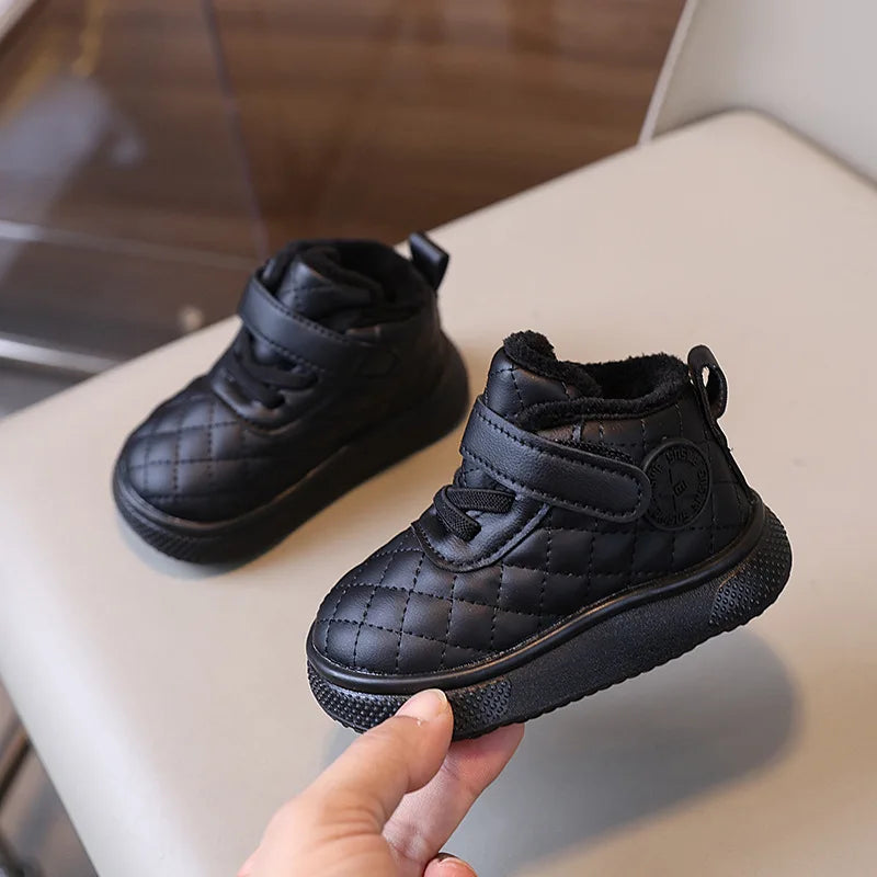 A close-up view of black toddler winter snow boots with a quilted texture and soft sole being held by a hand.