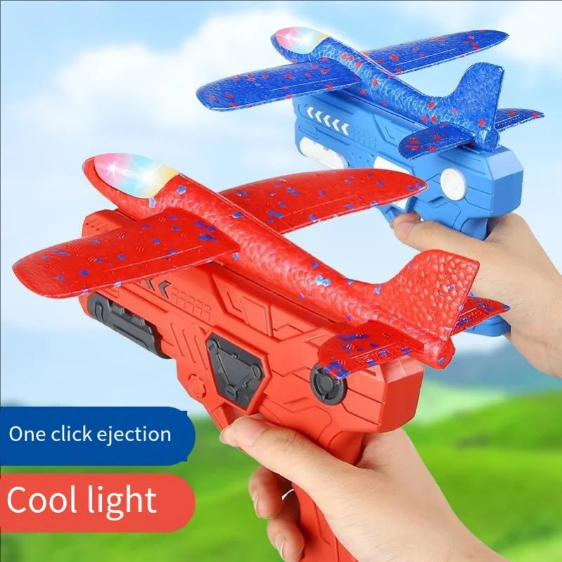 A hand holds an orange foam glider catapult toy gun with a red wing and blue accents, demonstrating one click ejection and co
