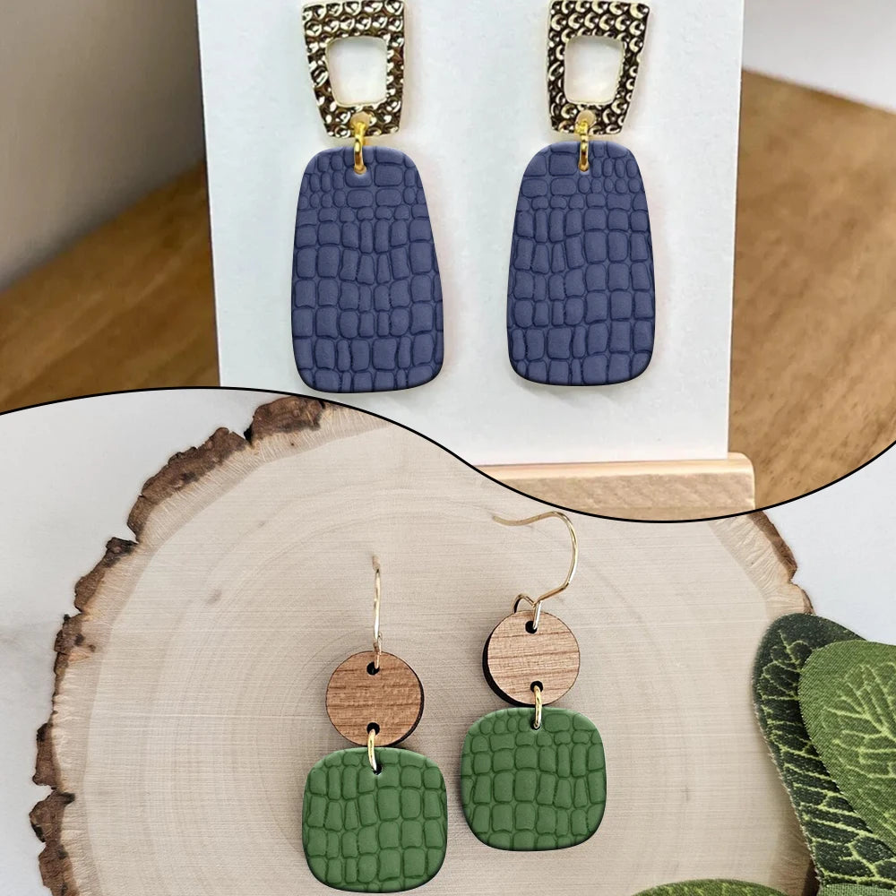 Pair of handmade jewelry earrings featuring textured clay rollers in slate blue and olive green.