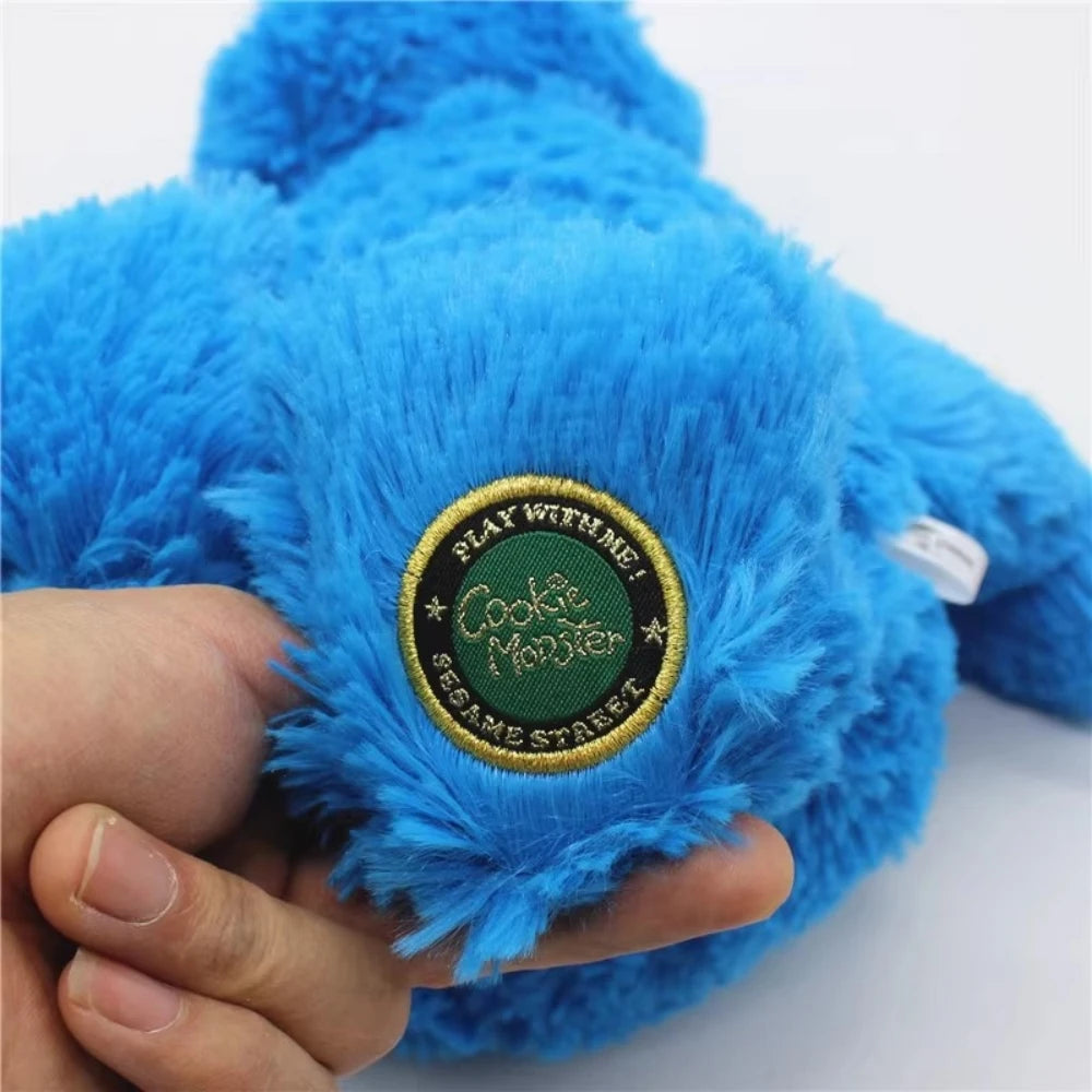 A hand holds a bright blue Cookie Monster plush toy with a circular green tag.