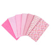 A stack of seven pink and floral patterned cotton fabric squares for quilting and patchwork.
