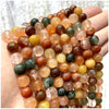 A hand holds a collection of natural stone beads including amethyst, garnet, and labradorite in various earthy tones.