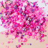 A pile of mixed resin rhinestone pearls in various shades of pink and purple scattered on a light surface.