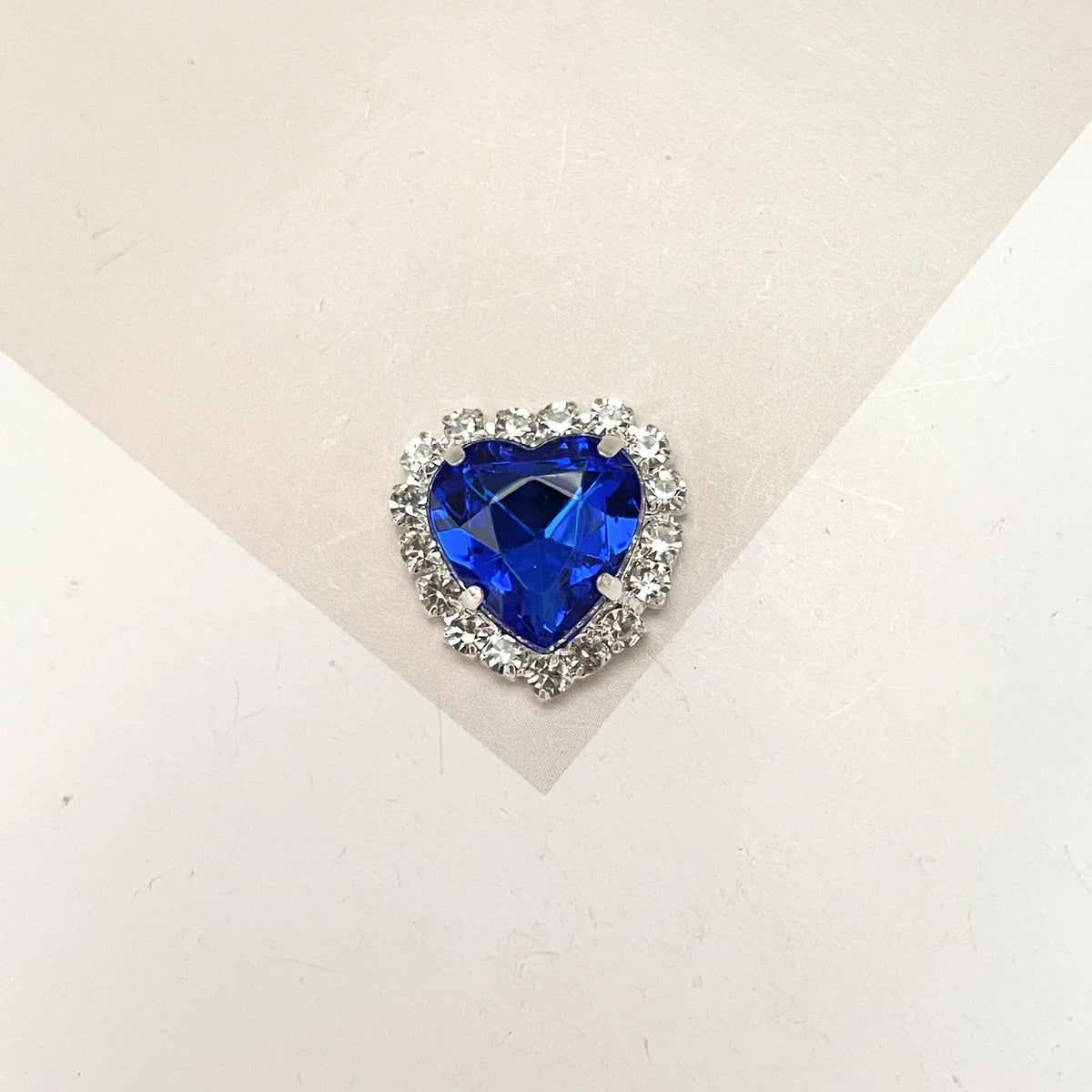 A brilliant blue heart-shaped gemstone surrounded by clear rhinestones.