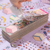 A hand is pouring a stack of 3D landscape stickers into a box, showing the colorful collection.