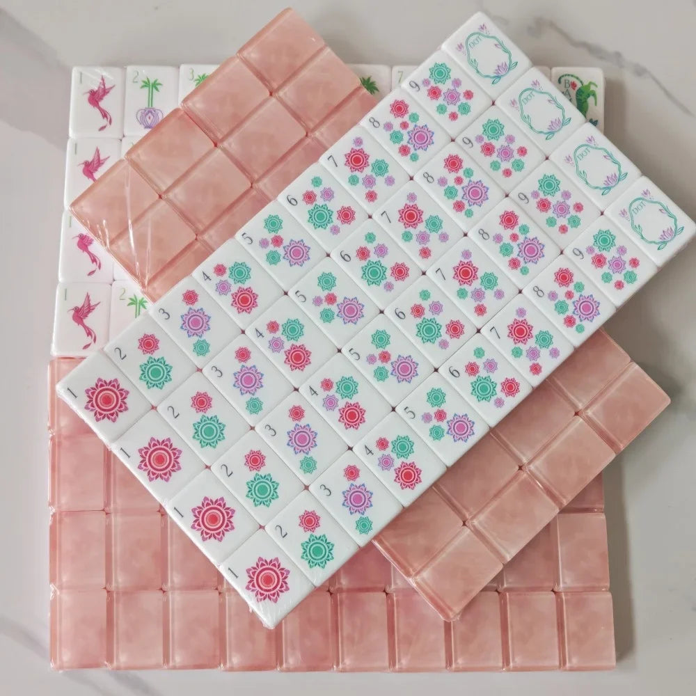 A set of pink acrylic mahjong tiles arranged in a grid, showing various patterns and colors.