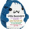 A blue and white crochet plush toy with a smiling face and a message encouraging resilience to ride the waves.