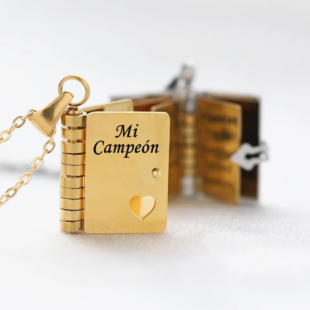 A gold engraved pendant necklace set featuring a book design with the text Mi Campeón and a heart.