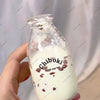 A hand holds a glass bottle containing white liquid and small red pieces, labeled Chiboki drink cup toy.