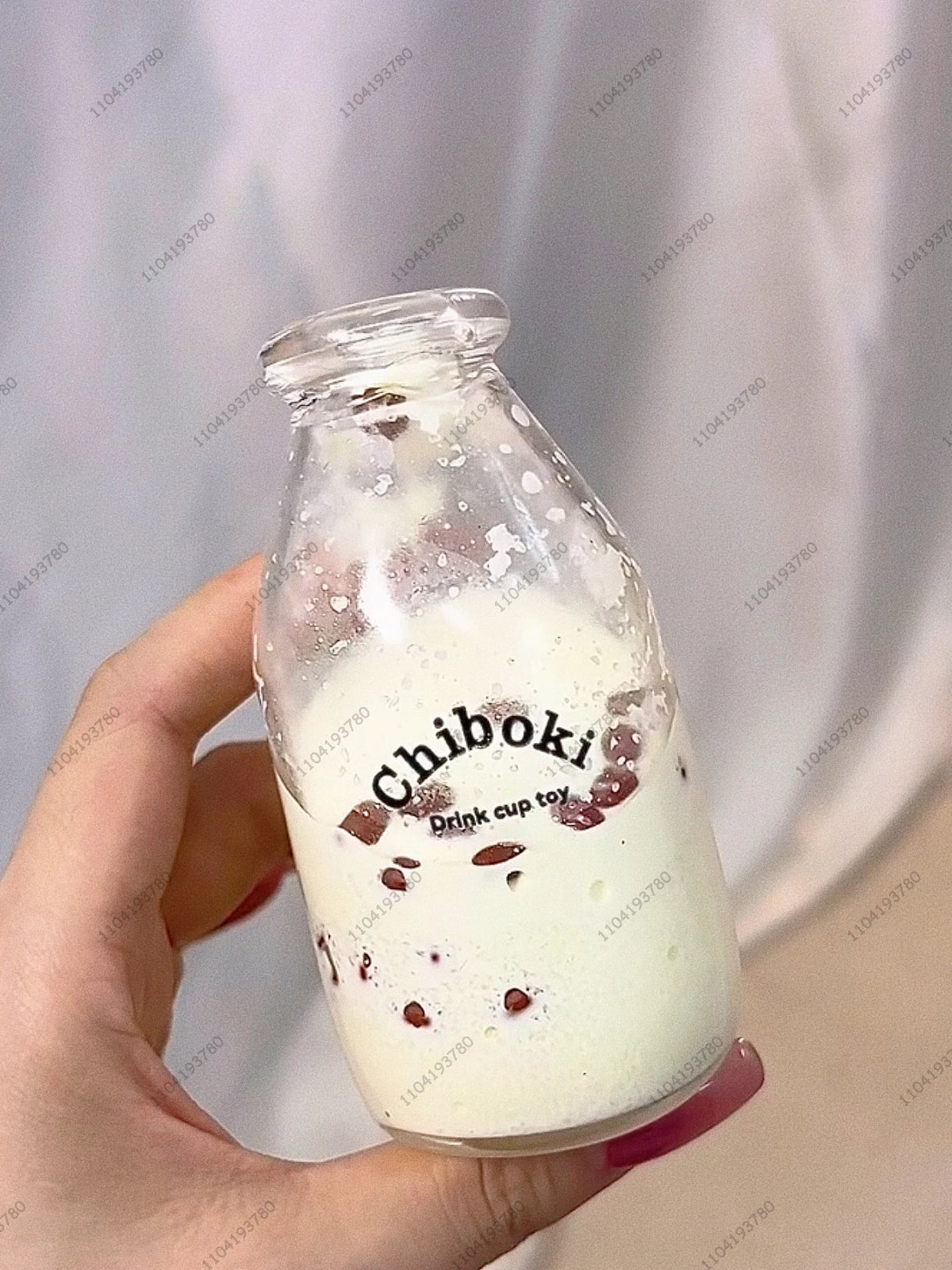 A hand holds a glass bottle containing white liquid and small red pieces, labeled Chiboki drink cup toy.