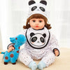 A baby doll wearing a panda hat and a matching romper set, sitting next to a blue dinosaur toy.