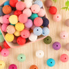 A collection of assorted colored silicone beads in various sizes arranged in a pink bowl.