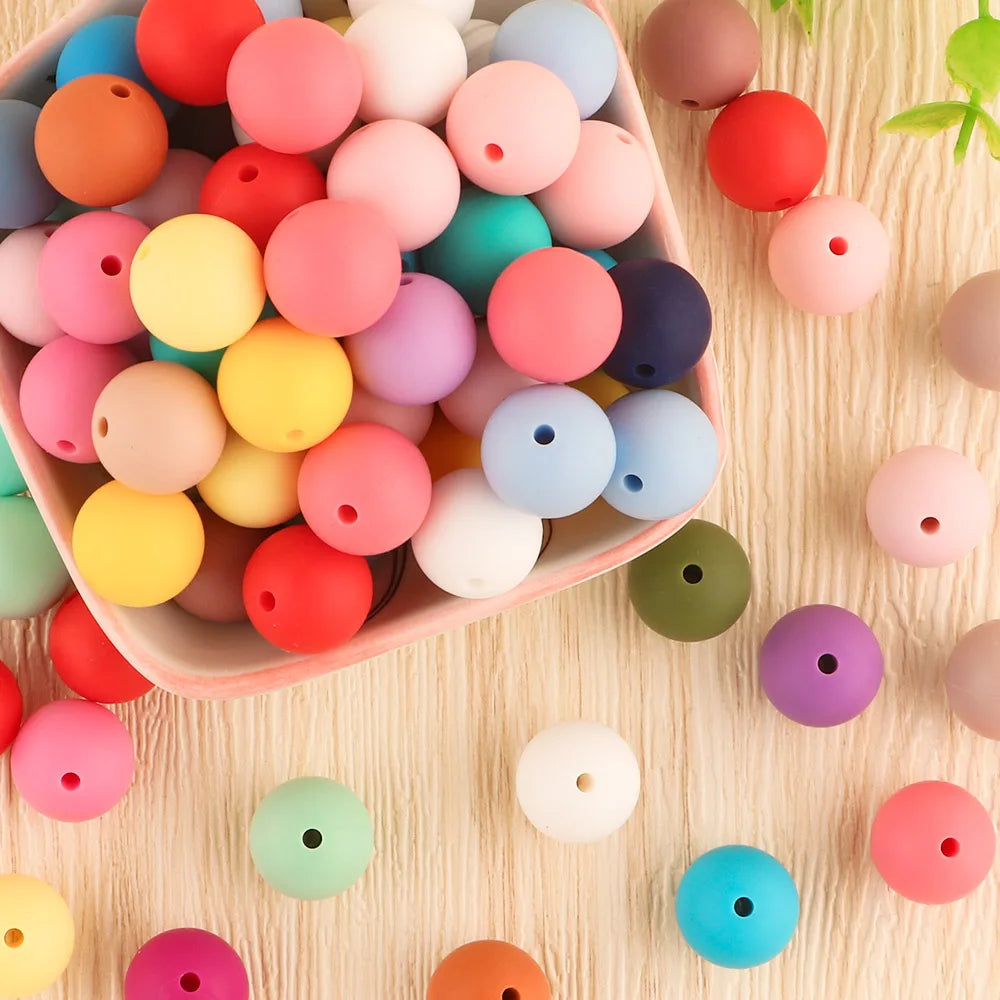 A collection of assorted colored silicone beads in various sizes arranged in a pink bowl.