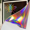 Holographic vinyl roll featuring a colorful bee design displayed against a window.