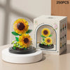 A white glass dome containing a miniature flower garden with yellow and orange flowers and green leaves, displayed next to it