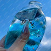 A hand holds a clear glass bottle filled with blue liquid and small bubbles, used as a squishy stress ball.