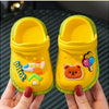 A pair of bright yellow children's clogs with orange and green accents are held by a hand.
