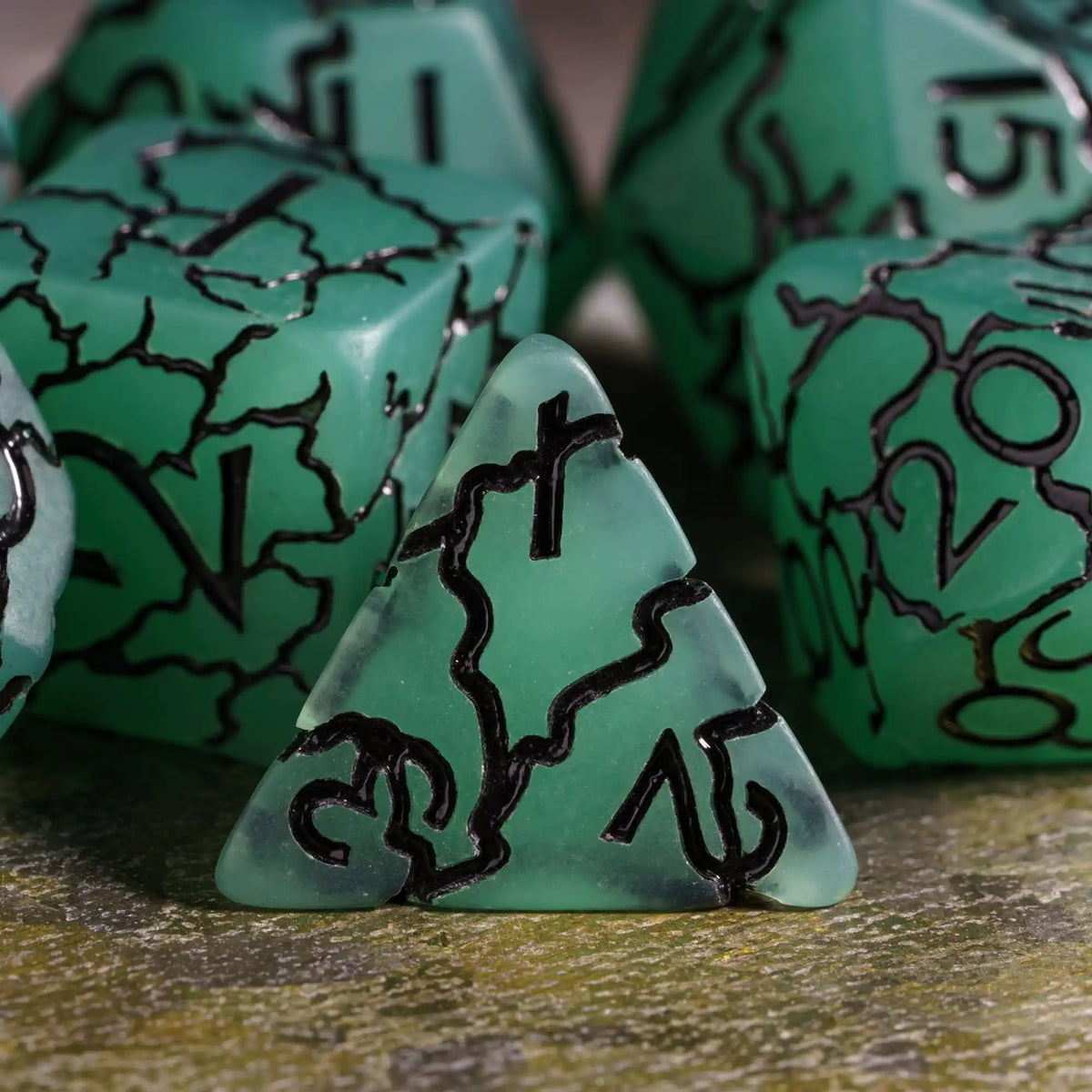 A close-up of a green frosted crack resin polyhedral dice set with black markings, including a triangular die.
