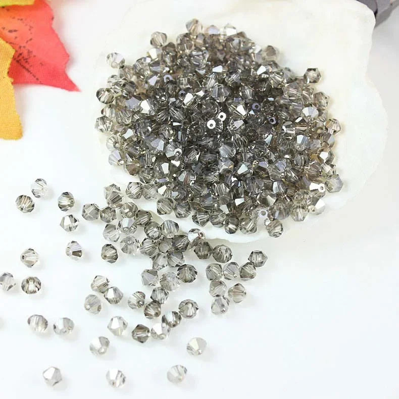 A pile of faceted gray and clear crystal beads is displayed on a white surface.