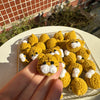 A collection of handcrafted yellow crochet animal keychains, including rabbits, chicks, cats, and dogs, displayed on a plate.