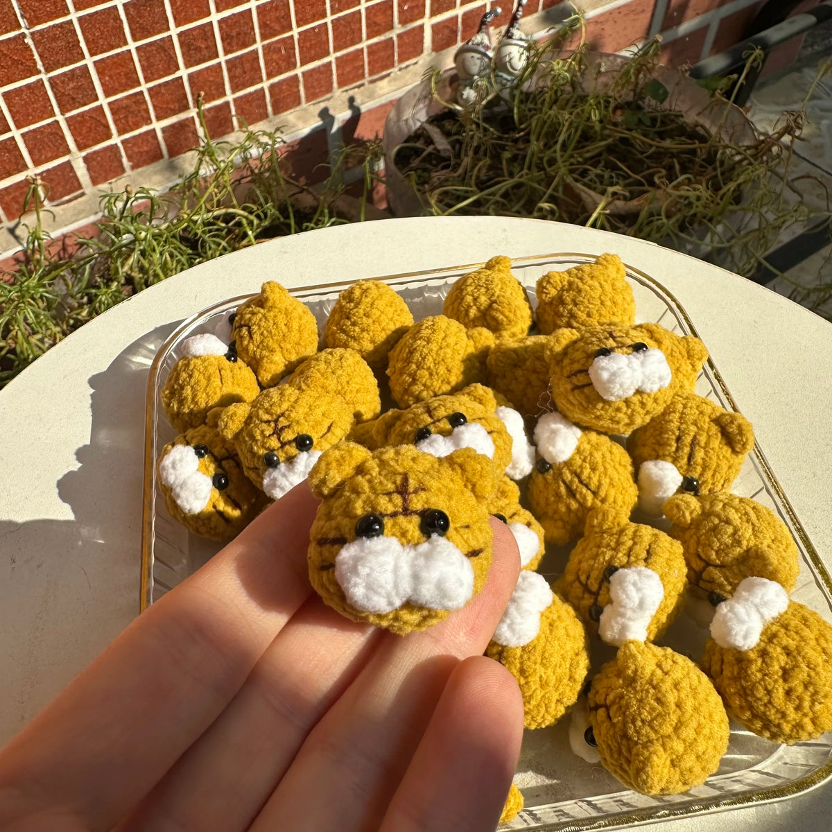 A collection of handcrafted yellow crochet animal keychains, including rabbits, chicks, cats, and dogs, displayed on a plate.