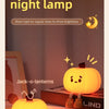 A glowing yellow pumpkin night lamp illuminates Jack-o'-lanterns on a wooden surface.