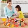 A child and parent interact with a mini barbecue pretend play set featuring various food items like sausages and vegetables.