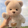 A hand is holding a white teddy bear plush with a knitted dress against a bright sky background.