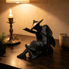 A dark, 3D printed samurai warrior figurine with a sword is displayed on a wooden surface next to a lit candle.