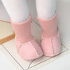 Pair of pink knit baby booties with white socks displayed on a white surface.