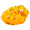 A bright yellow jelly putty with black specks and a green, cartoonish face on top.