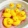 A hand holds several bright yellow silicone duck bath toys floating in water.