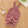 A pair of dusty rose corduroy baby cotton overalls with adjustable straps lying on a wooden surface.