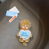 A small, fluffy brown plush toy with a smiling face is attached to a keychain charm for bags and keys.
