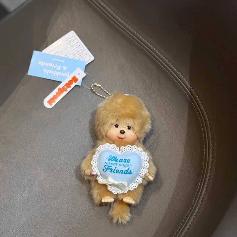 A small, fluffy brown plush toy with a smiling face is attached to a keychain charm for bags and keys.