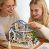 A woman and a girl look at a seaside beach house miniature dollhouse kit with an LED light.