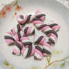 A collection of pink and white polymer clay marshmallow charms shaped like striped candies arranged on a white plate.