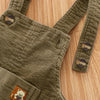 Olive green baby cotton overalls with adjustable straps lying on a wooden surface.