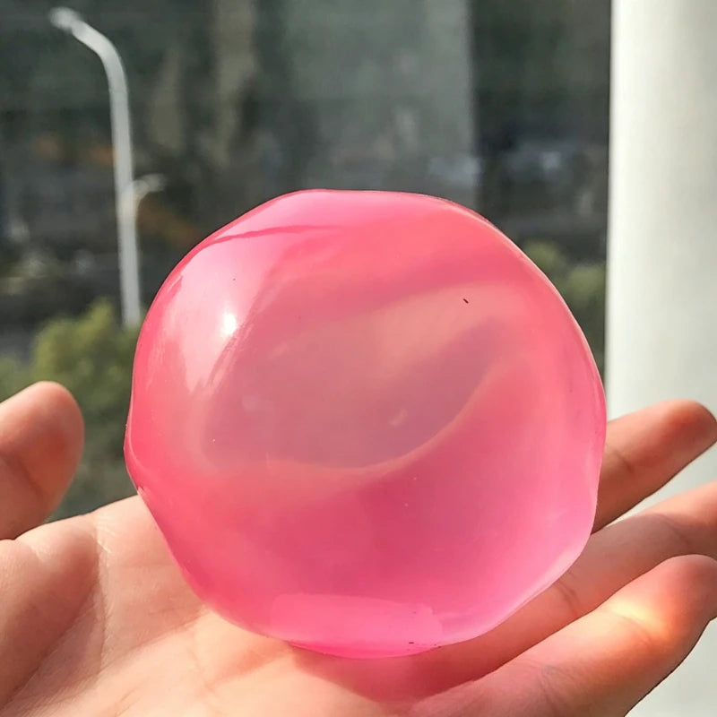 A hand holds a smooth, translucent pink squishy stress relief toy with swirling internal colors.