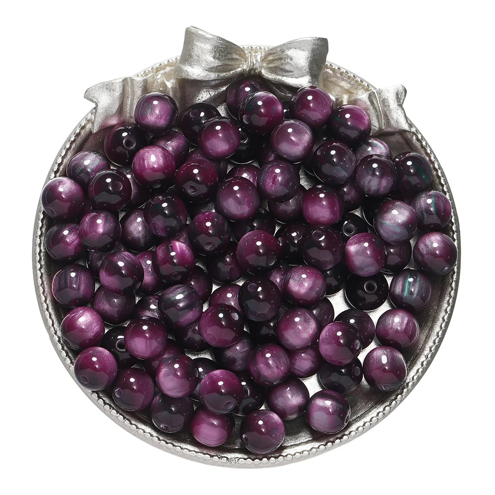 A pile of round, deep purple glitter cat eye resin beads in a silver-toned dish.