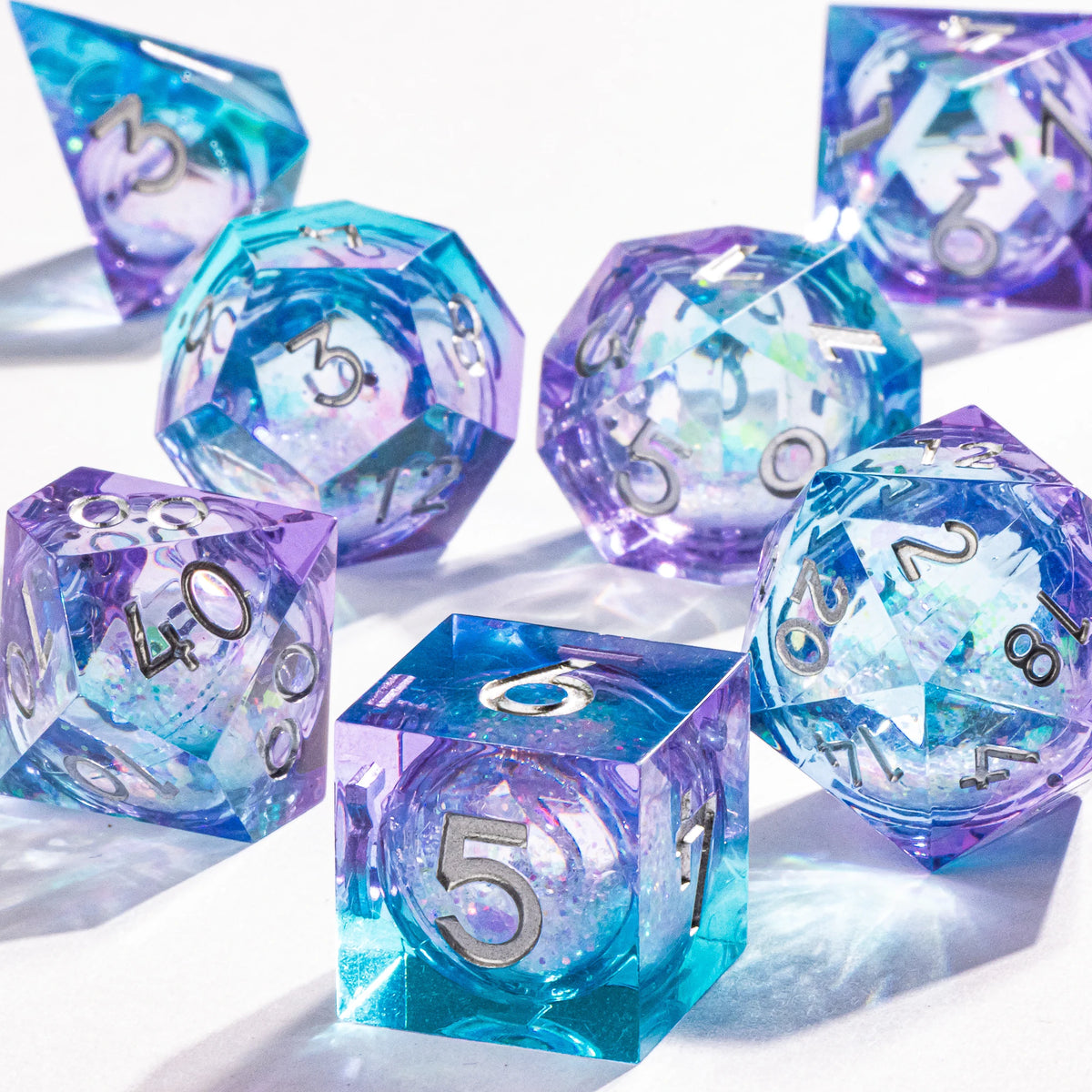 A collection of handmade liquid core polyhedral dice in shades of blue and purple with a galaxy finish