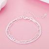 A silver snake chain bracelet is displayed on a pink surface.